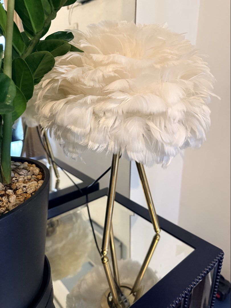 White Feather Shade Table Lamp with Gold Legs (Category: Lighting) located in Quezon City. Submitted by yourheaduhunter (Listing ID 1466225640, Image 1). Description: - Fluffy white feather lampshade for a chic, aesthetic look - Slender gold-toned metal tripod stand for stability and style - Emits a cozy warm yellow glow when lit up - Perfect statement piece for bedside tables or living room corners.
