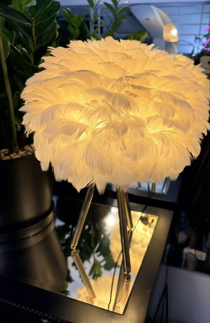 White Feather Shade Table Lamp with Gold Legs (Category: Lighting) located in Quezon City. Submitted by yourheaduhunter (Listing ID 1466225640, Image 2). Description: - Fluffy white feather lampshade for a chic, aesthetic look - Slender gold-toned metal tripod stand for stability and style - Emits a cozy warm yellow glow when lit up - Perfect statement piece for bedside tables or living room corners.