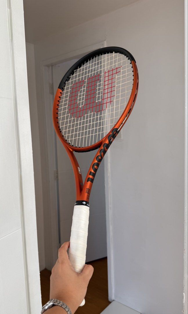 Wilson Burn 100ULS V5 Tennis Racket (Category: Racket and Ball Sports) located in San Fernando. Submitted by _gzel (Listing ID 1465983677, Image 1). Description: - Model: Wilson Burn 100ULS V5 - Color: Vibrant orange and black - Condition: Clean frame (no dent or scratches). Scratch on the bumper guard only (replaceable) - Setup: Strung - Grip: Original black grip tape still intact. With white overgrip - Performance: Solid option for players want