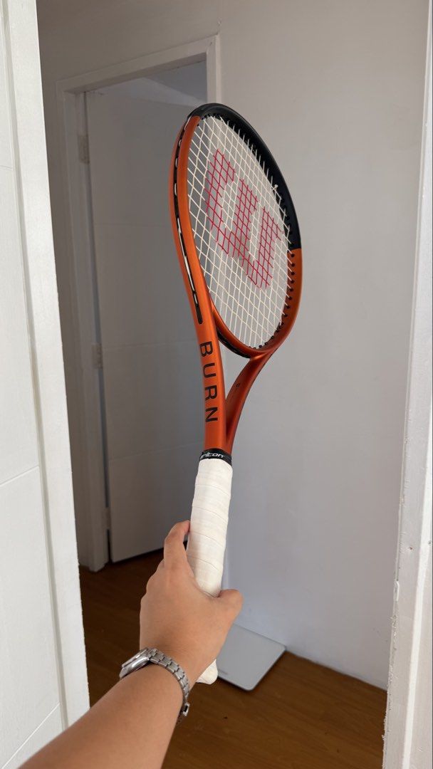 Wilson Burn 100ULS V5 Tennis Racket (Category: Racket and Ball Sports) located in San Fernando. Submitted by _gzel (Listing ID 1465983677, Image 2). Description: - Model: Wilson Burn 100ULS V5 - Color: Vibrant orange and black - Condition: Clean frame (no dent or scratches). Scratch on the bumper guard only (replaceable) - Setup: Strung - Grip: Original black grip tape still intact. With white overgrip - Performance: Solid option for players want