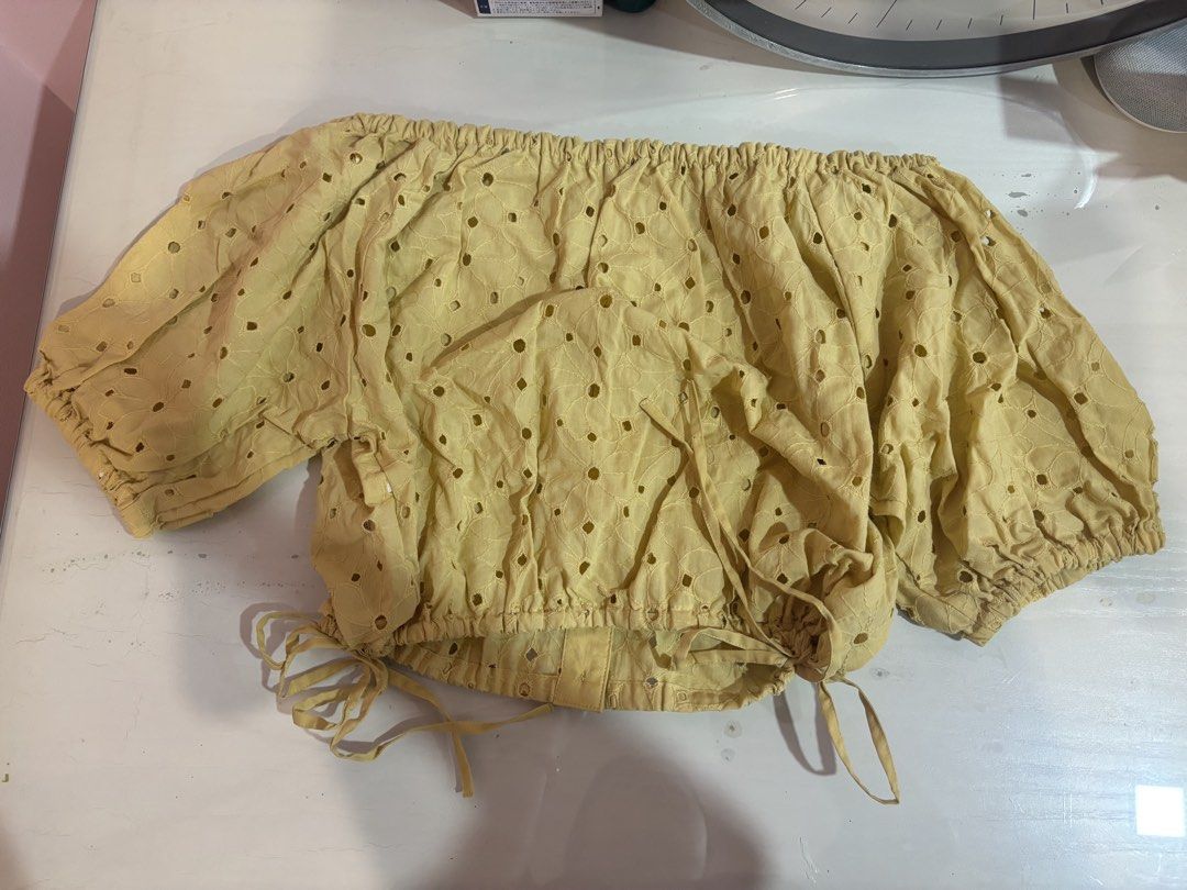 Yellow off-shoulder eyelet crop top with buttons (Category: Blouses) located in Manila. Submitted by beaswardrobe (Listing ID 1466321041, Image 2). Description: - Color: Bright mustard yellow - Design: All-over eyelet cutout pattern - Details: Puff sleeves, elasticated neckline, and front button placket - Fit: Adjustable tie strings at the bottom hem - Material: Lightweight fabric - Condition: Great styling piece for sunny days.