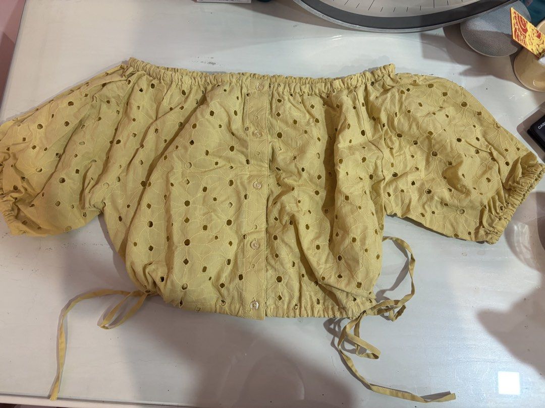 Yellow off-shoulder eyelet crop top with buttons (Category: Blouses) located in Manila. Submitted by beaswardrobe (Listing ID 1466321041, Image 1). Description: - Color: Bright mustard yellow - Design: All-over eyelet cutout pattern - Details: Puff sleeves, elasticated neckline, and front button placket - Fit: Adjustable tie strings at the bottom hem - Material: Lightweight fabric - Condition: Great styling piece for sunny days.