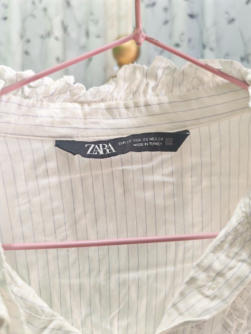 ZARA Striped Ruffle High Neck Blouse (Category: Blouses) located in Caloocan City. Submitted by _misskaye (Listing ID 1466161282, Image 3). Description: - Brand: ZARA - Size: XS - Color: White with subtle blue vertical stripes - Details: High ruffled neck, button-down front with vertical ruffle trims, long sleeves - Material: Lightweight fabric - Origin: Made in Turkey - Condition/Use: Great for layering or wearing solo to work or casual outings.