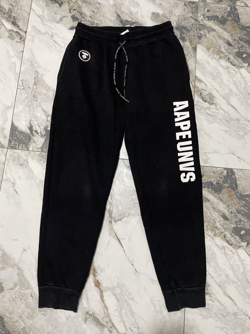 AAPE BY A BATHING APE® UNVS Moonface Logo Sweatpants (Category: Joggers) located in Antipolo. Submitted by divineyyy69 (Listing ID 1466525180, Image 1). Description: Authentic AAPE BY A BATHING APE® UNVS graphic joggers/sweatpants in black. Features the distinct vertical AAPEUNVS varsity-style text block on the left leg, a front circular rubberized moonface badge, and customized branded premium metal aglets. The back pocket sports an oversized ic