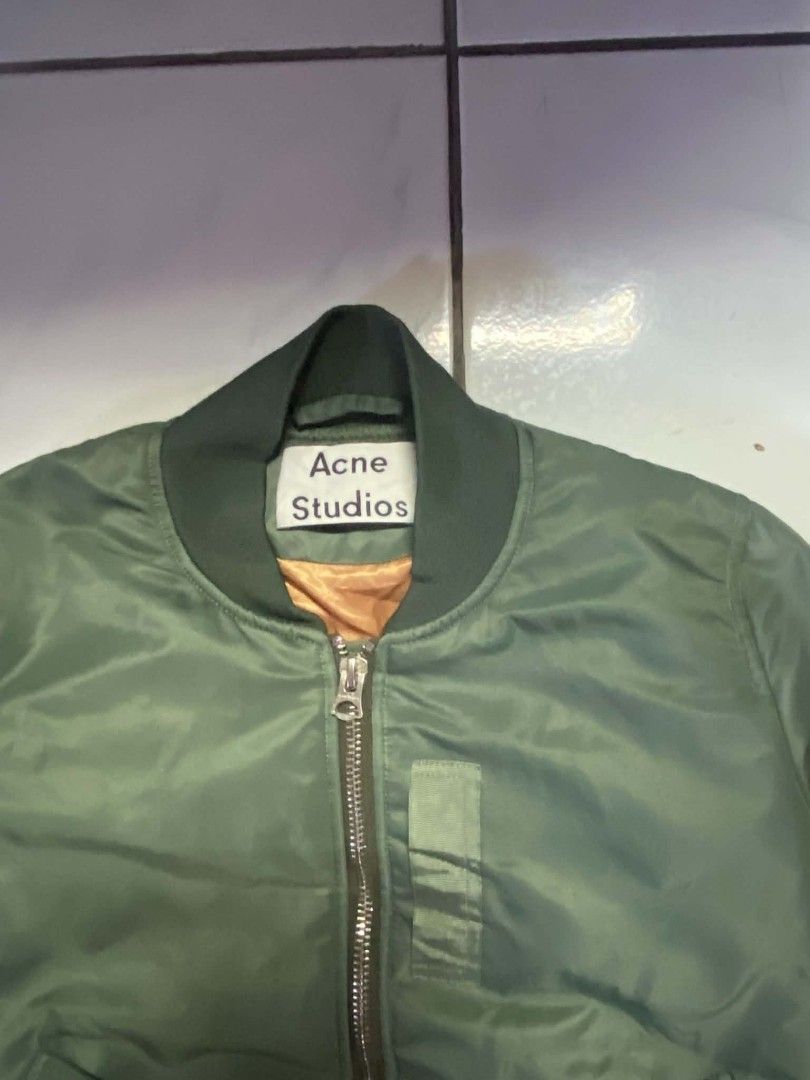Acne Studios Green Bomber Jacket (Category: Coats, Jackets and Outerwear) located in Angeles City. Submitted by pkthreadz (Listing ID 1466370407, Image 2). Description: - Brand: Acne Studios - Color: Olive green with bright orange lining - Size: 34 - Dimes: 20.5x24 - Details: Ribbed collar, cuffs, and hem; metal front zipper with dual pulls - Pockets: Zippered sleeve utility pocket and angled snap-flap front pockets - Condition: Clean outer shell