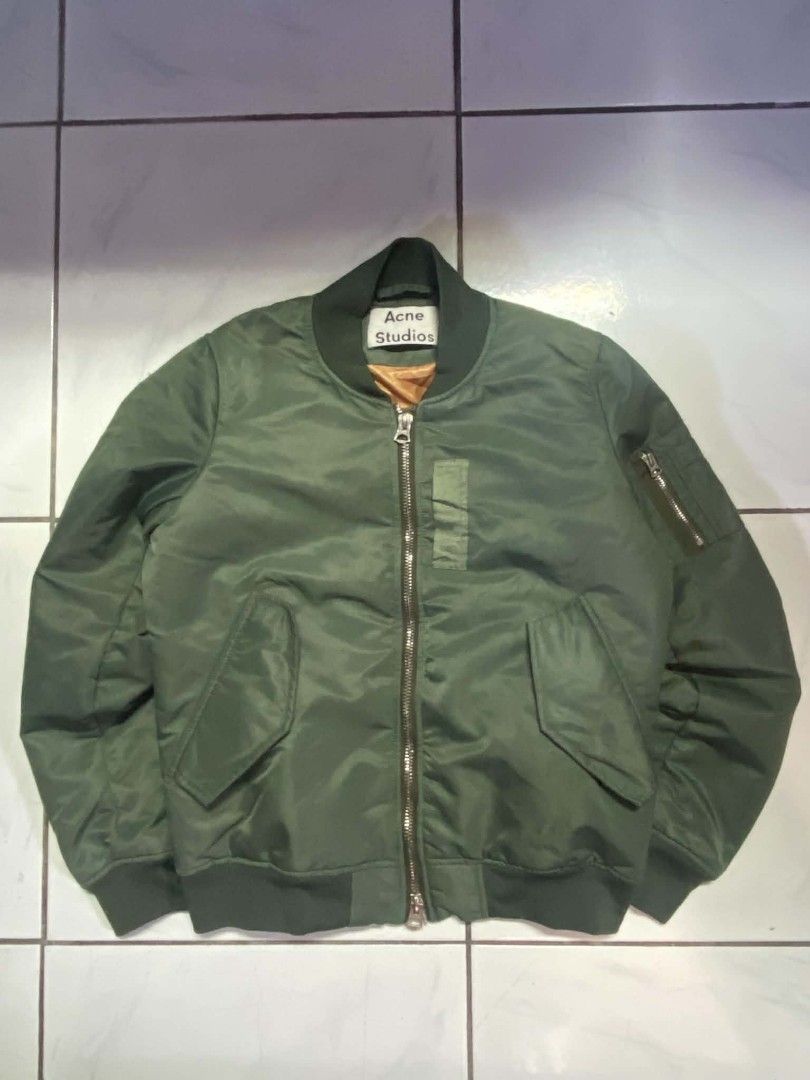 Acne Studios Green Bomber Jacket (Category: Coats, Jackets and Outerwear) located in Angeles City. Submitted by pkthreadz (Listing ID 1466370407, Image 1). Description: - Brand: Acne Studios - Color: Olive green with bright orange lining - Size: 34 - Dimes: 20.5x24 - Details: Ribbed collar, cuffs, and hem; metal front zipper with dual pulls - Pockets: Zippered sleeve utility pocket and angled snap-flap front pockets - Condition: Clean outer shell