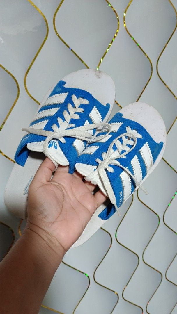 Adidas Gazelle Slides Blue White (Category: Slippers & Slides) located in Manila. Submitted by zariyah.1986 (Listing ID 1466439465, Image 1). Description: - Item: Adidas Gazelle slides - Color: Blue and white with classic three stripes and decorative laces - Size: US 7 / UK 6 / FR 39 / JP 245 / CHN 240 - Material: Suede upper with white footbed - Details: Adidas branding and Gazelle text on the side, made in Vietnam (Date code: 05/24) - Condition