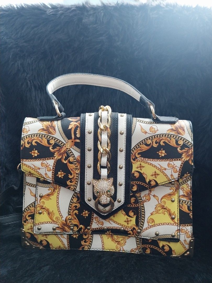 ALDO Barob (Category: Shoulder Bags) located in Bacoor. Submitted by sereeen.cm (Listing ID 1466437000, Image 2). Description: - Bold black, white, and yellow baroque print - Eye-catching rhinestone leopard head clasp closure - Chic gold-tone chain detail on the front flap - Structured faux leather build with a spacious interior - Includes a top handle and an adjustable black shoulder strap - Protective gold metal corner brackets on the base.