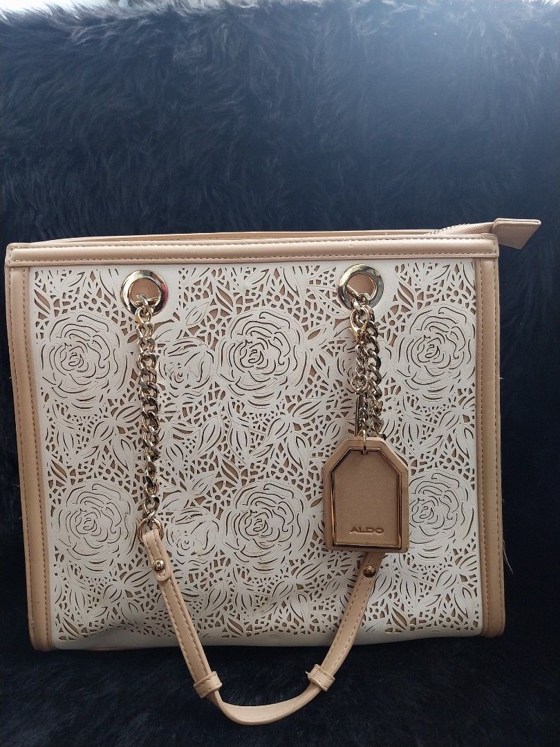 ALDO Botanika (Category: Shoulder Bags) located in Bacoor. Submitted by sereeen.cm (Listing ID 1466437137, Image 1). Description: - Brand: ALDO - Color: Elegant beige and cream combination - Design: Beautiful laser-cut floral pattern on the front panel with clean piped edging - Straps: Luxurious gold-tone chain handles combined with comfortable faux leather - Closure: Secure top zipper closure - Extras: Includes a matching branded luggage tag acc