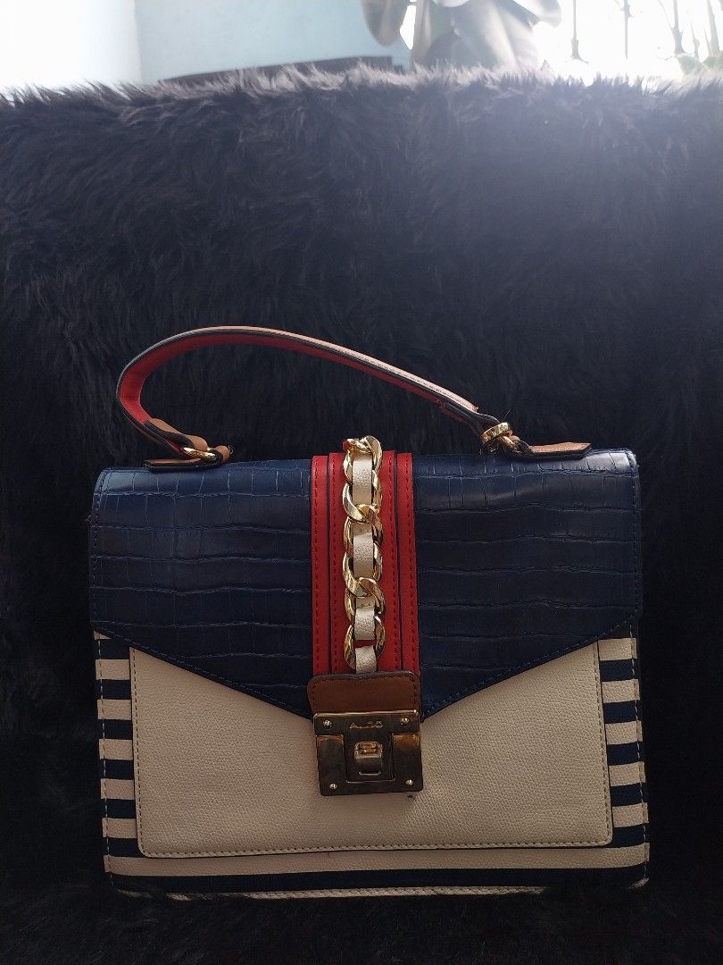 ALDO Glendaa (Category: Tote Bags) located in Bacoor. Submitted by sereeen.cm (Listing ID 1466436623, Image 2). Description: - Brand: ALDO - Design: Nautical navy and white stripes with faux-croc flap and red band - Details: Gold chain accent and detachable brown tassel charm - Features: Structured shape, secure turn-lock closure, and stylish top handle - Perfect statement bag to elevate casual or resort outfits!.