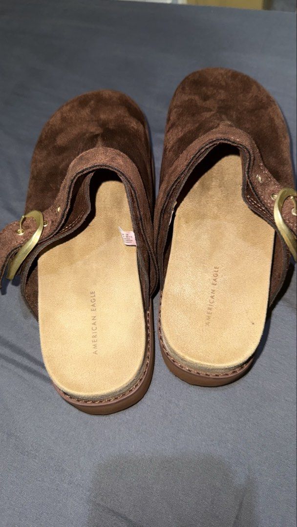 American Eagle Brown Suede Clogs Size 8 (Category: Slippers and slides) located in Andop. Submitted by nobleangel (Listing ID 1466350320, Image 2). Description: - Brand: American Eagle - Style: Slip-on clogs with adjustable side buckle and metallic hardware (Style #6913-200) - Size: US 8 / EUR 38.5 / MX 25 / CN 250 - Material: Suede upper texture with wavy ridged sole pattern underneath - Condition: Clean footbeds with stamped brand logo - Origin