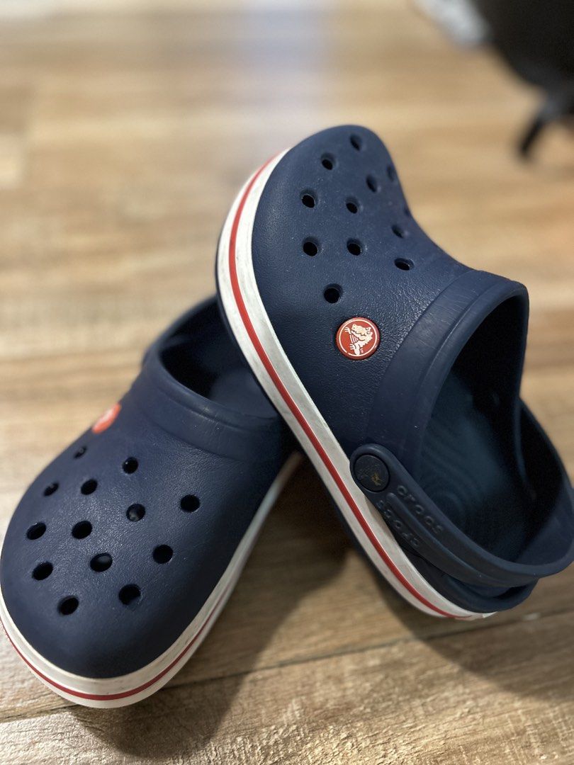 Authentic Crocs Navy Blue Kids Clogs Size J1 (Category: Babies & Kids Fashion) located in San Fernando. Submitted by gisellelynn77 (Listing ID 1466562690, Image 2). Description: - Color: Navy blue with red and white trim along the midsole - Size: J1 (marked on the bottom) - Origin: Made in Indonesia - Design: Classic slip-on style for quick and easy wear - Comfort: Iconic ventilation holes on top for breathability - Fit: Movable heel strap featur