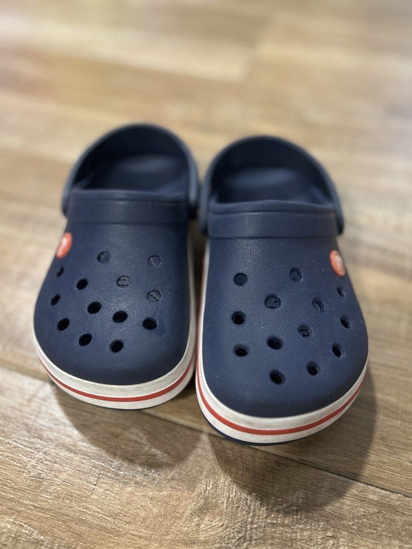Authentic Crocs Navy Blue Kids Clogs Size J1 (Category: Babies & Kids Fashion) located in San Fernando. Submitted by gisellelynn77 (Listing ID 1466562690, Image 1). Description: - Color: Navy blue with red and white trim along the midsole - Size: J1 (marked on the bottom) - Origin: Made in Indonesia - Design: Classic slip-on style for quick and easy wear - Comfort: Iconic ventilation holes on top for breathability - Fit: Movable heel strap featur