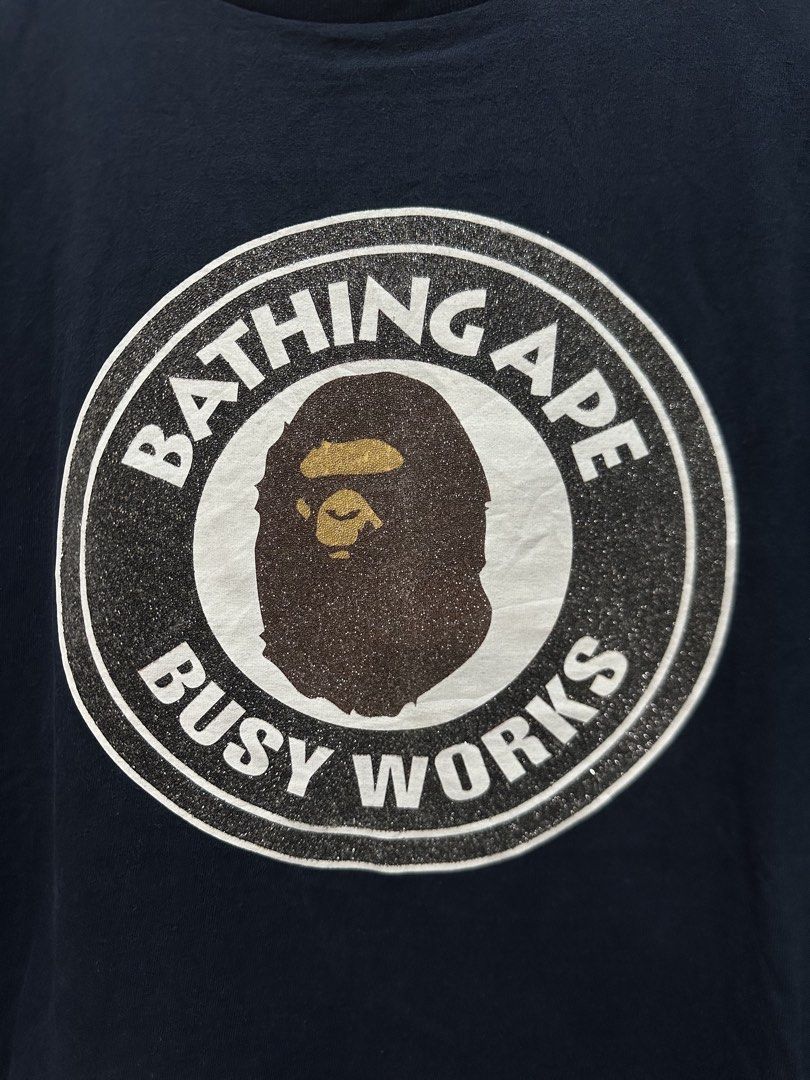 BAPE "Bathing Ape Busy Works" Glittered (Authentic) (Category: Tshirts & Polo Shirts ) located in Manila. Submitted by ylsrarities (Listing ID 1466545701, Image 2). Description: Authentic A Bathing Ape (BAPE) “Busy Works” graphic t-shirt in navy blue. Features the iconic Ape Head circle logo printed with silver glitter text detailing on the front. Brand: A Bathing Ape / BAPE Color: Navy Blue / White / Gold / Silver Glitter Size: XL (Tagged XL / 1