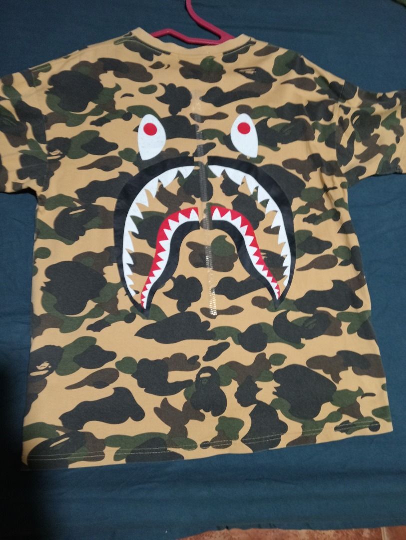 BAPE Yellow Camo WGM Shark Tee (Category: Tshirts & Polo Shirts ) located in Caloocan City. Submitted by yazzielux (Listing ID 1466348307, Image 1). Description: - Brand: BAPE (A Bathing Ape) - Design: Yellow camo with signature back shark face graphic and large WGM chest lettering - Fit: Standard streetwear fit - Details: Short sleeves, crew neck - Authenticity: Includes inner neck tags and wash care labels - Condition: Brand new / Excellent qua