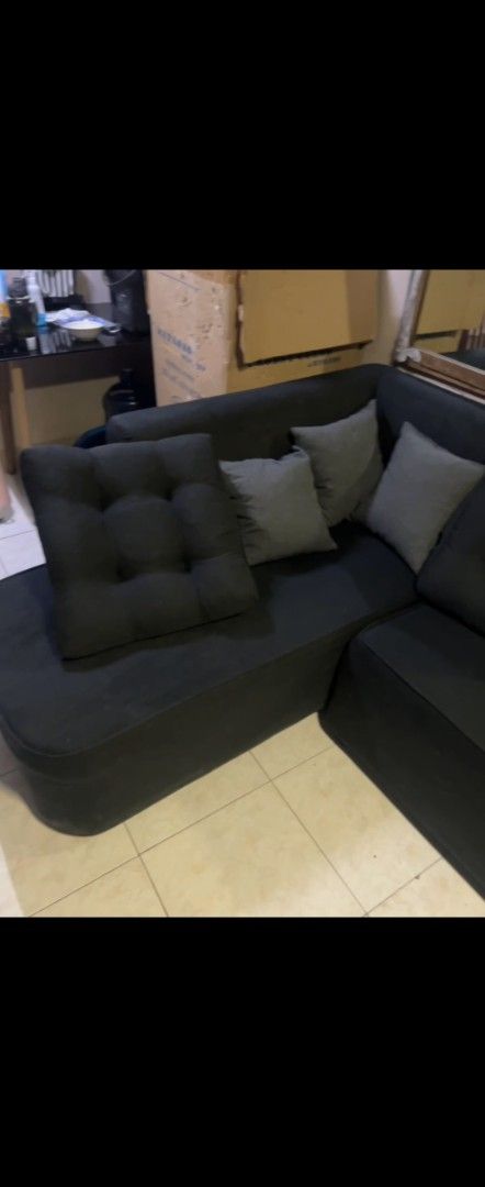 Black L-shaped sectional sofa with matching cushions (Category: Sofas) located in Mandaluyong City. Submitted by bambi14 (Listing ID 1466430443, Image 2). Description: - Type: Black fabric L-shaped sectional sofa with matching movable ottoman / Only bought las January 2026 - Includes: Grey scatter cushions and one large tufted black floor cushion - Condition: Clean upholstery with minimal wear, very comfortable - Ideal for: Living room spaces and