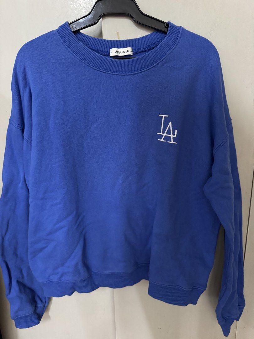 Blue LA Dodgers Logo Sweatshirt (Category: Coats, Jackets and Outerwear) located in Manila. Submitted by kaiahs.preloved (Listing ID 1466384775, Image 1). Description: -M-L - Color: Bright royal blue - Design: Small embroidered white LA Dodgers logo on the chest - Fit: Relaxed fit with long drop-shoulder sleeves - Features: Ribbed crew neckline, cuffs, and hem - Material: Soft fabric, great for casual layering on cooler days.