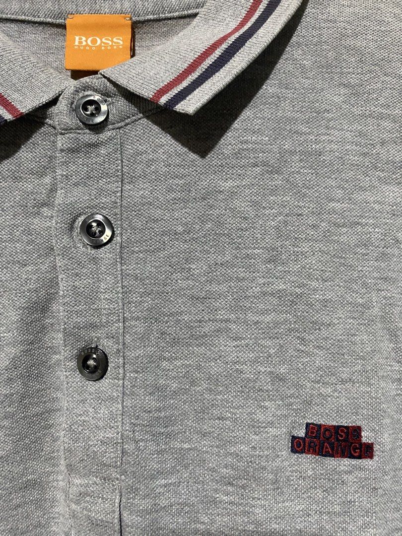 Boss Orange Grey Polo Shirt Size M (Category: Tshirts & Polo Shirts ) located in Manila. Submitted by jfrancis18 (Listing ID 1466355721, Image 3). Description: Grey Boss Orange polo shirt in size M. Short sleeves, classic three-button placket. Striped collar detail in red and navy. Embroidered logo patch on the chest, plus a small metal brand plaque near the hem. Soft cotton fabric, breathable and comfortable. Great basic for casual wear or smart