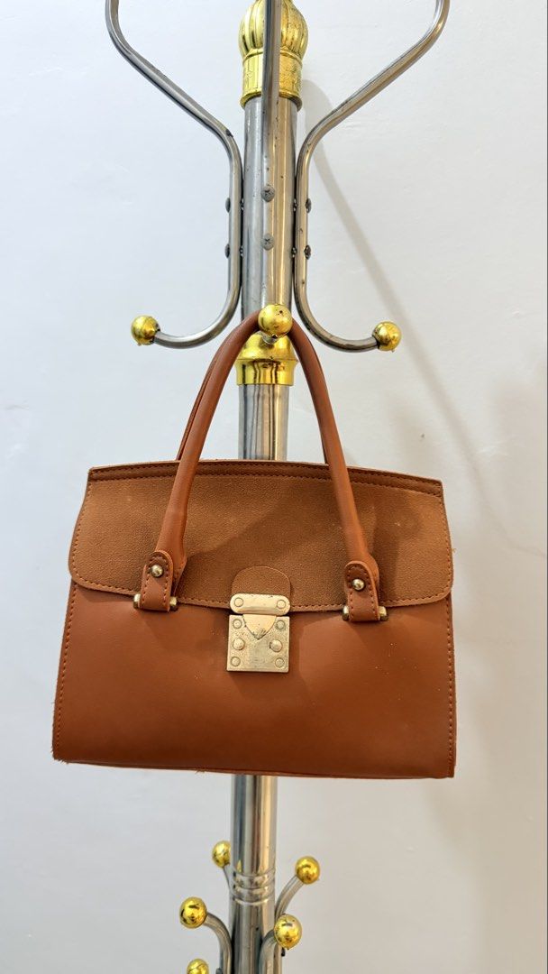 Brown Leather Handbag with Metal Lock (Category: Luxury Bags & Wallets) located in Manila. Submitted by laxamanapa81165 (Listing ID 1466539152, Image 2). Description: - Color: Tan brown - Material: Smooth leather with suede flap panel - Hardware: Metallic push-lock closure and sturdy metal studs - Handles: Dual top handles - Design: Structured rectangular body with a clean silhouette - Use: Perfect for daily use, work, or casual outings.