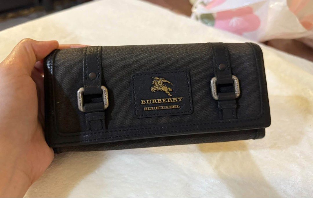 Burberry blue label long wallet (Category: Luxury Bags & Wallets) located in San Jose del Monte. Submitted by mightyhawk.59282e (Listing ID 1466385976, Image 1). Description: • Brand: Burberry Blue Label (a line formerly produced in Japan under license) • Material: Black canvas exterior with leather trim and buckle details • Design: Rectangular long wallet silhouette with dual decorative strap-and-buckle accents and a rectangular Burberry Blue La