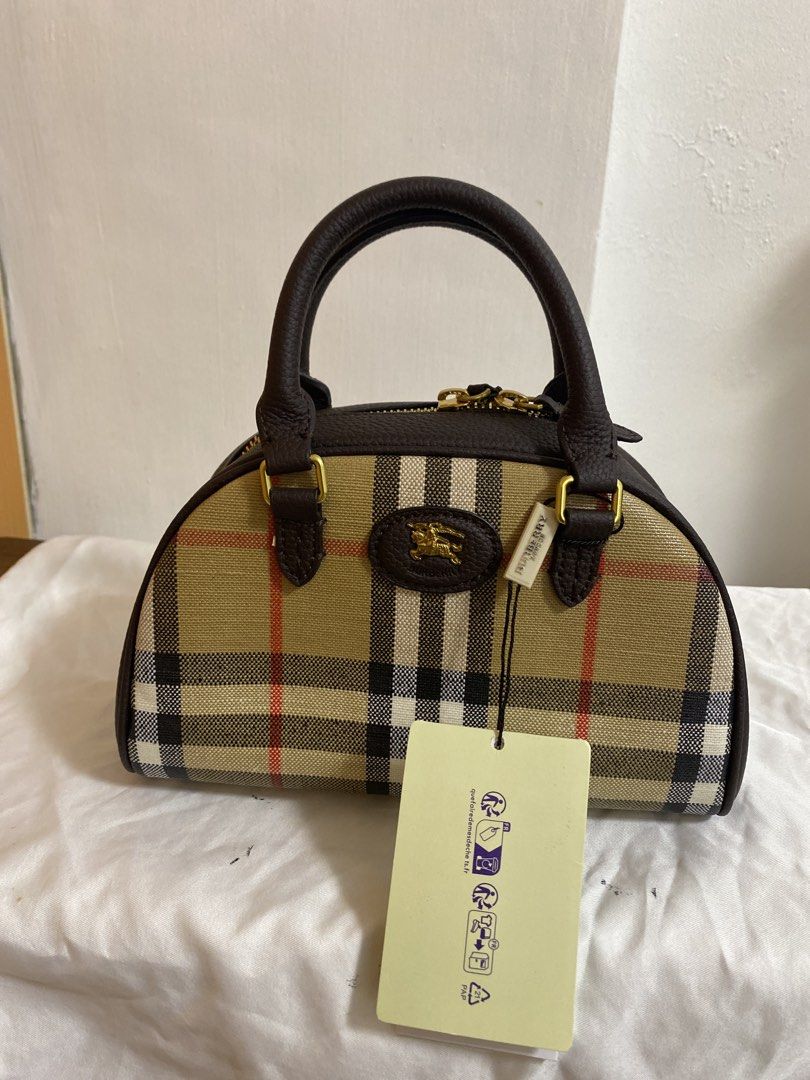 Burberry House Check Bowling Handbag (Category: Luxury Bags & Wallets) located in Pasig City. Submitted by raine.lb (Listing ID 1466403629, Image 1). Description: - Authentic Burberry handbag in iconic check pattern (beige, red, black, and white) - Premium dark brown leather trim and rolled top handles - Secure gold-tone zipper closure - Classic equestrian knight logo plaque on the front - Structured flat bottom design - Includes original tag att