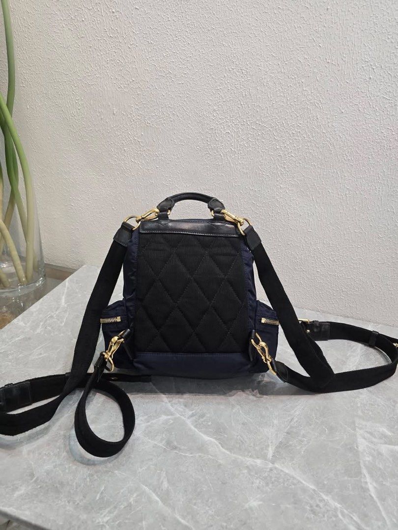 Burberry Nylon Rucksack Backpack Navy Blue (Category: Backpacks) located in Baao. Submitted by jodelmancera21 (Listing ID 1466358401, Image 3). Description: - Authentic Burberry navy blue nylon backpack - Luxurious black leather top handle and trim details - Elegant gold-tone hardware throughout - Secure front flap with buckle closures and drawstring pull - Convenient front zipper pocket and side pockets - Comfortable quilted back panel with adju