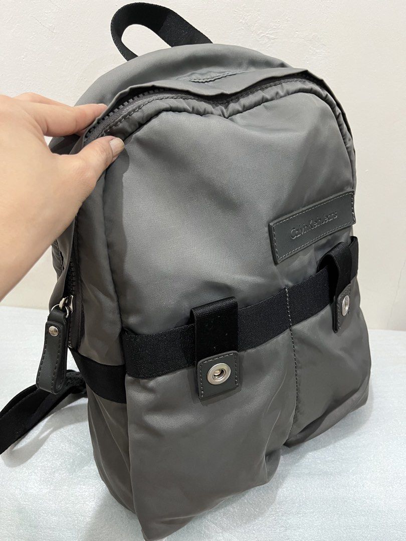 Calvin Klein Jeans Grey Nylon Backpack (Category: Backpacks) located in Talisay. Submitted by cherylu (Listing ID 1466503626, Image 2). Description: Calvin Klein Jeans backpack in grey nylon material. Black webbing strap across the front with snap button tabs. Silver-tone zipper pullers stamped with CKJ logo. Black fabric lining inside the main compartment. Adjustable black shoulder straps. Clean exterior and interior..