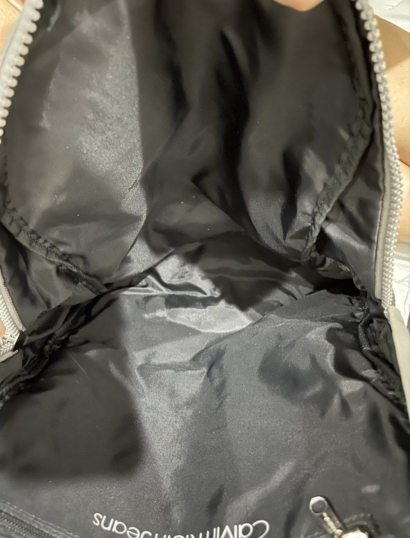 Calvin Klein Jeans Grey Nylon Backpack (Category: Backpacks) located in Talisay. Submitted by cherylu (Listing ID 1466503626, Image 3). Description: Calvin Klein Jeans backpack in grey nylon material. Black webbing strap across the front with snap button tabs. Silver-tone zipper pullers stamped with CKJ logo. Black fabric lining inside the main compartment. Adjustable black shoulder straps. Clean exterior and interior..