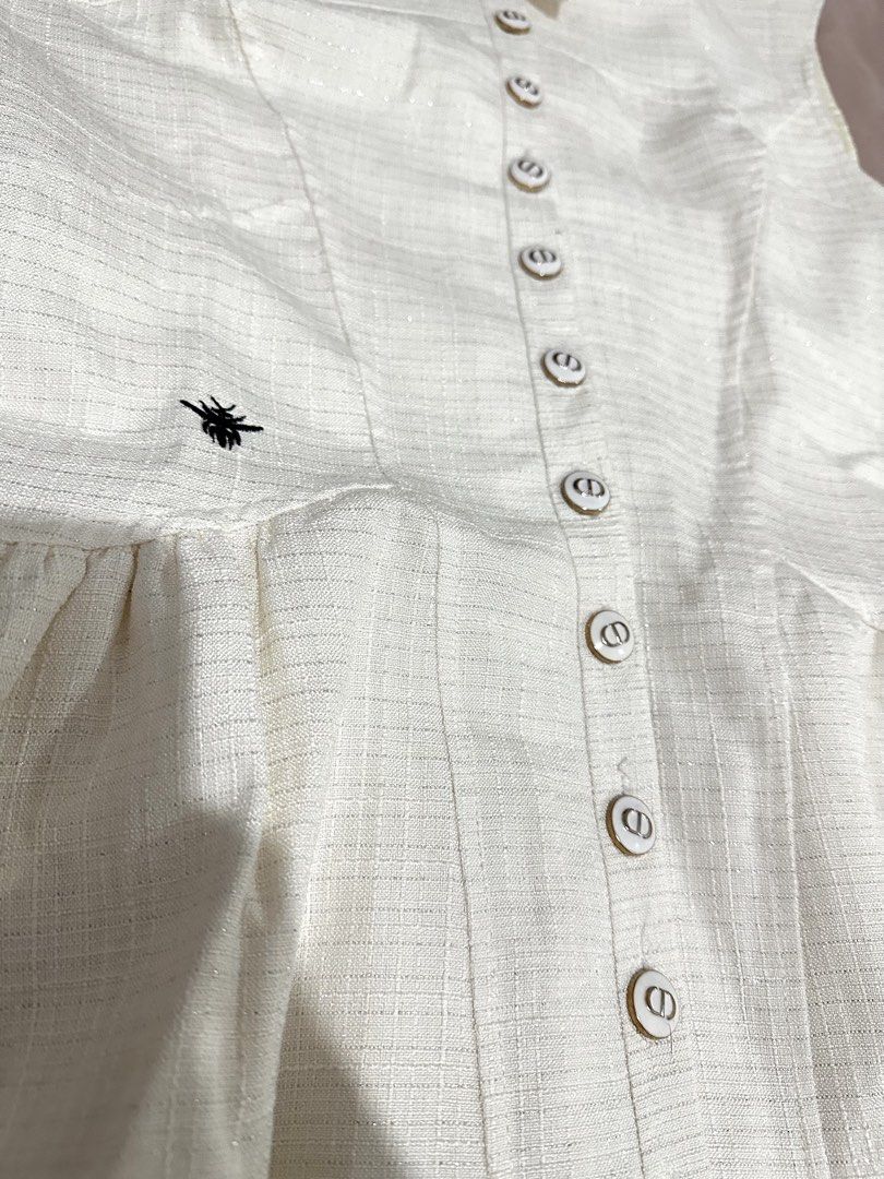 CD Cream Sleeveless Collared Button-Down Dress with Bee Embroidery CD buttons (Category: Dresses) located in Manila. Submitted by everythingsale101 (Listing ID 1466441040, Image 3). Description: - Color: Light Cream - Style: Sleeveless collared dress with dropped waist and flared pleated skirt - Details: Full front button closure featuring luxury CD monogram hardware on every button - Accent: Distinct black bee embroidery on the right side - Fabr