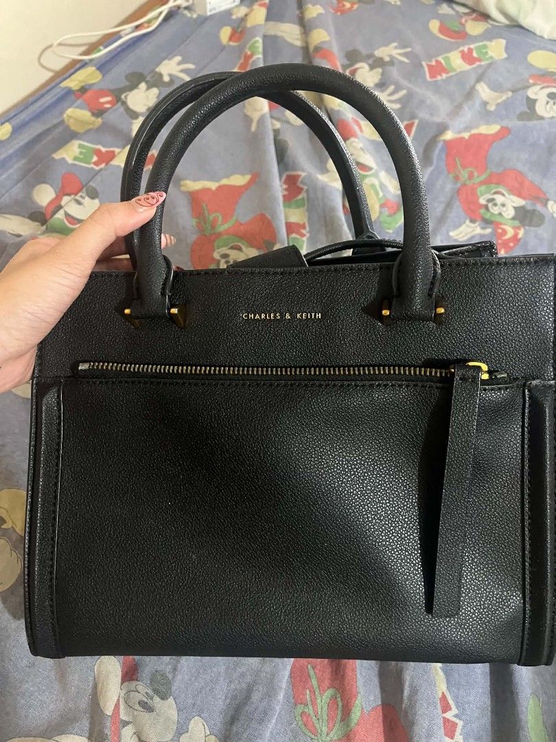 Charles & Keith Black Tote Handbag (Category: Tote Bags) located in Manila. Submitted by margag0o3o76600 (Listing ID 1466473456, Image 1). Description: Black Charles & Keith structured handbag with dual top handles. Gold-tone hardware throughout. Front zip pocket with pull tab. Multiple interior compartments including a zippered middle partition and snap button closure at the top. Clean black lining inside. Classic everyday size for work or casua