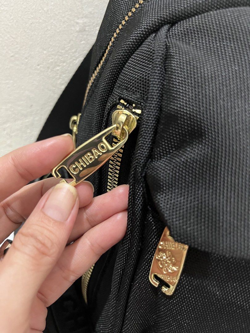 CHIBAO Black Nylon Mini Backpack Gold Hardware (Category: Backpacks) located in Talisay. Submitted by cherylu (Listing ID 1466536311, Image 3). Description: Black nylon backpack from CHIBAO with gold-toned metal accents. Front zipped pocket and main compartment. Signature branded fabric lining inside with extra slip and zip pockets. Adjustable straps feature woven CHIBAO lettering. Clean hardware and sturdy fabric construction throughout..