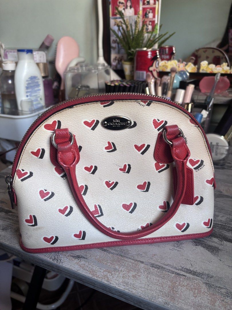 💖 AUTHENTIC COACH MINI SIERRA DOME SATCHEL💖 (Category: Luxury Bags & Wallets) located in Caloocan City. Submitted by isabellz._miwiw (Listing ID 1466339507, Image 1). Description: - Authentic Coach dome satchel - Cream colorway with playful red and black heart pattern - Vibrant red leather dual top handles - Silver-toned hardware with front Coach logo plate - Secure zip-around closure - Includes original Coach hangtag - Compact size, perfect fo