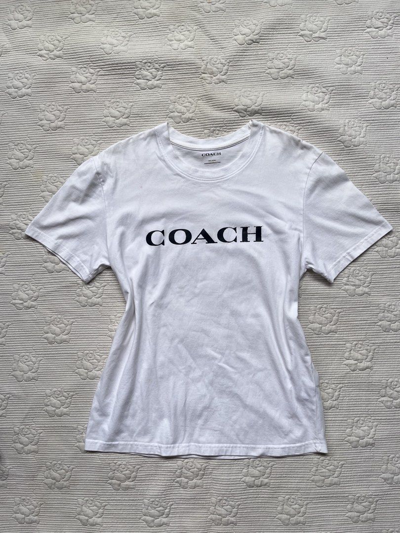Coach White T-Shirt Small (Category: Shirts) located in Alabel. Submitted by geragarhea13830 (Listing ID 1466407849, Image 1). Description: - Brand: Coach - Color: White with bold black logo lettering - Size: Small (165/88A) - Material: 100% clean cotton (Made in India) - Fit/Style: Short sleeves, classic crew neck - Condition: Excellent, easy to pair with any casual outfit.