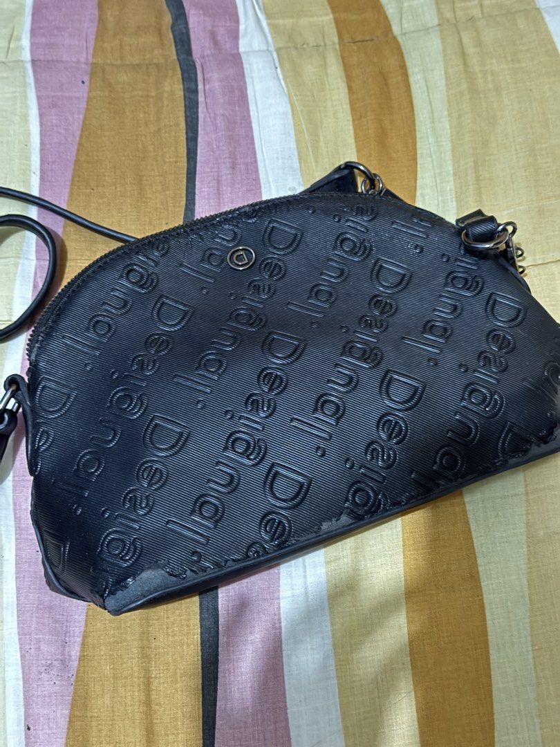 Desigual Black Embossed Logo Crossbody Bag (Category: Cross-body Bags) located in Pasig City. Submitted by authentic_preloved_by_elca (Listing ID 1466455643, Image 1). Description: Authentic Desigual crossbody bag in black. All-over embossed logo pattern across the exterior. Zip closure on top with a smaller zip pocket on the front. Includes a detachable chain detail spelling Desigual with metal hardware. Interior tag intact with style code 20WAX