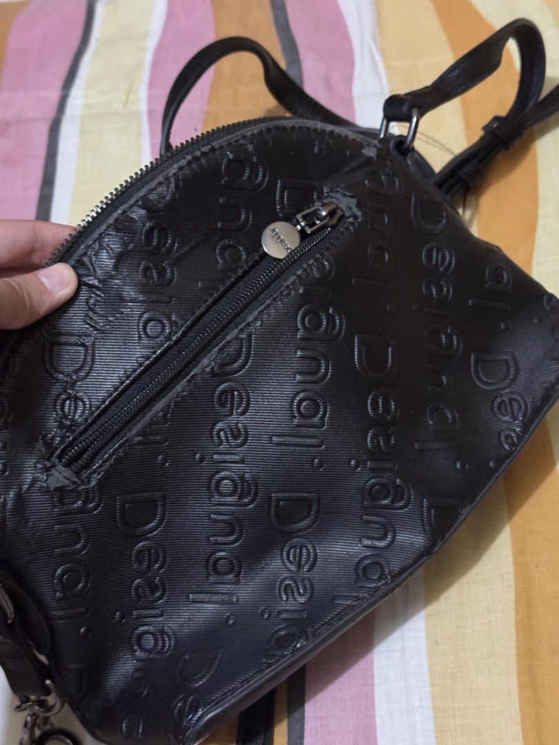 Desigual Black Embossed Logo Crossbody Bag (Category: Cross-body Bags) located in Pasig City. Submitted by authentic_preloved_by_elca (Listing ID 1466455643, Image 3). Description: Authentic Desigual crossbody bag in black. All-over embossed logo pattern across the exterior. Zip closure on top with a smaller zip pocket on the front. Includes a detachable chain detail spelling Desigual with metal hardware. Interior tag intact with style code 20WAX