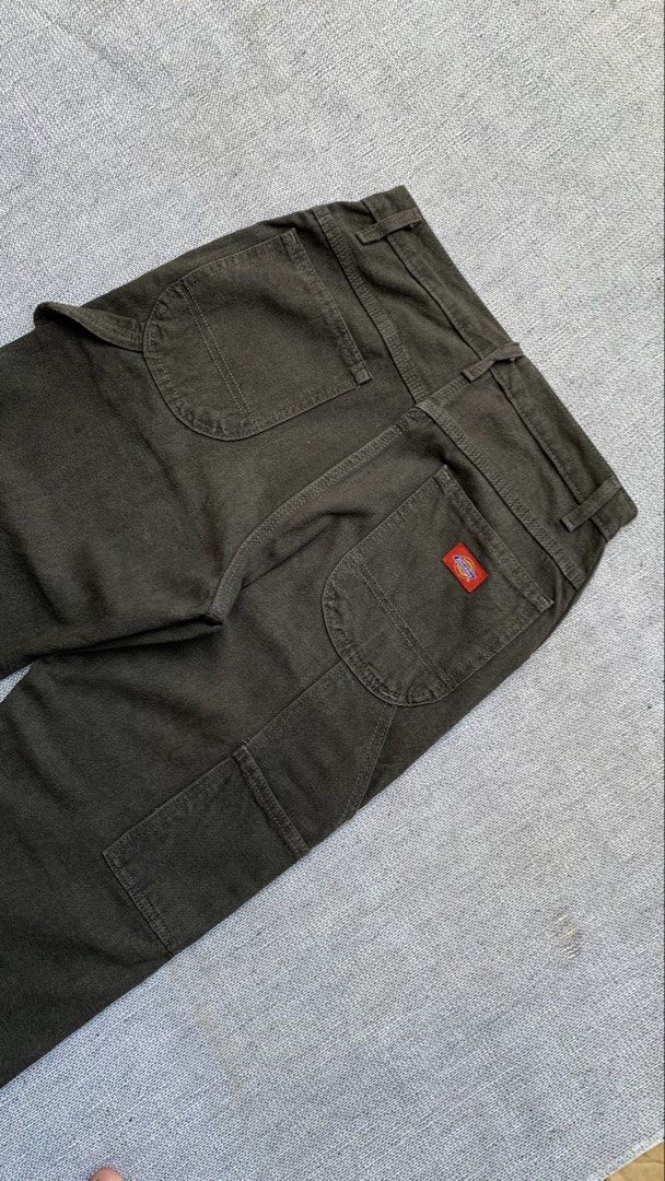 Dickies Olive Green Cargo Pants (Category: Trousers) located in Jamindan. Submitted by darinville30528 (Listing ID 1466415031, Image 1). Description: - Brand: Dickies - Style: Utility carpenter pants with relaxed straight leg - Color: Dark olive green - Material: Durable, heavy-duty canvas fabric - Features: Multiple tool pockets, side hammer loop, and metal button fly closure - Branding: Classic red and yellow Dickies logo patch on the back pock