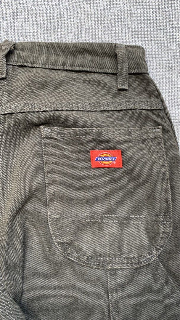 Dickies Olive Green Cargo Pants (Category: Trousers) located in Jamindan. Submitted by darinville30528 (Listing ID 1466415031, Image 2). Description: - Brand: Dickies - Style: Utility carpenter pants with relaxed straight leg - Color: Dark olive green - Material: Durable, heavy-duty canvas fabric - Features: Multiple tool pockets, side hammer loop, and metal button fly closure - Branding: Classic red and yellow Dickies logo patch on the back pock