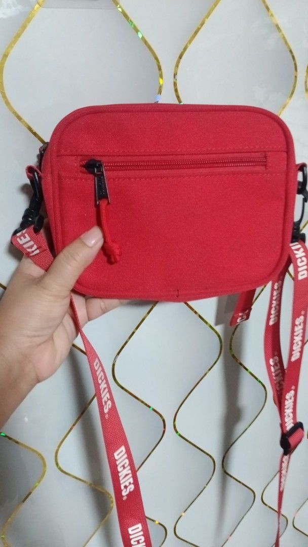 Dickies Red Crossbody Bag (Category: Sling Bags) located in Manila. Submitted by zariyah.1986 (Listing ID 1466475913, Image 2). Description: - Brand: Dickies - Color: Bright red with white embroidered logo - Material: Clean, sturdy canvas - Compartments: Zippered main compartment and handy front zipper pocket - Strap: Adjustable red strap with repeat Dickies branding - Interior: Dark lining with branded stamp - Condition: Great compact size for d