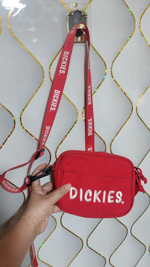 Dickies Red Crossbody Bag (Category: Sling Bags) located in Manila. Submitted by zariyah.1986 (Listing ID 1466475913, Image 1). Description: - Brand: Dickies - Color: Bright red with white embroidered logo - Material: Clean, sturdy canvas - Compartments: Zippered main compartment and handy front zipper pocket - Strap: Adjustable red strap with repeat Dickies branding - Interior: Dark lining with branded stamp - Condition: Great compact size for d