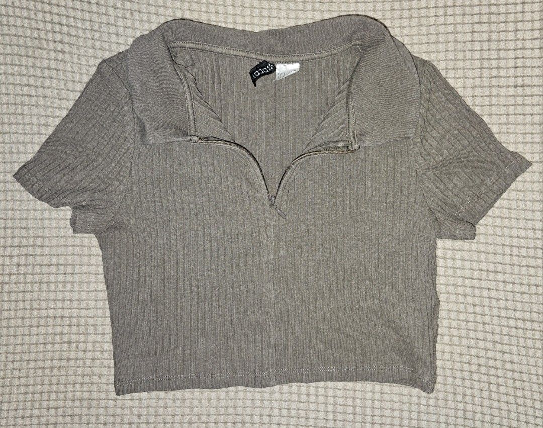 Divided H&M Ribbed Zip-Up Collared Crop Top (Category: Sleeveless) located in Marikina City. Submitted by lacheriecloset (Listing ID 1466468629, Image 1). Description: Divided by H&M crop top in a brownish-grey shade. Ribbed knit material with short sleeves and a collared neckline. Front features a quarter zip closure. Size S tag attached inside the collar. Simple everyday basic top, easy to style with high-waisted jeans or skirts..