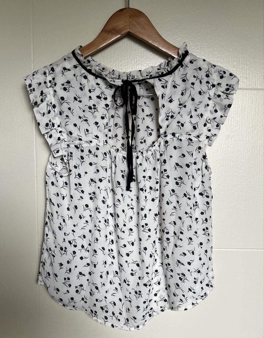 Floral Short Sleeve Blouse (Category: Blouses) located in Pasig City. Submitted by jsyrgt (Listing ID 1466430978, Image 2). Description: White Floral Blouse Condition: 10/10 Brand New with Marshalls store tag attached. Small yellowish stain on the side seam near the armhole area (shown in the last photo). Design: High neckline trimmed in black, open back with a black tie closure Details: Floral print blouse with short flutter sleeves Styling: Gre