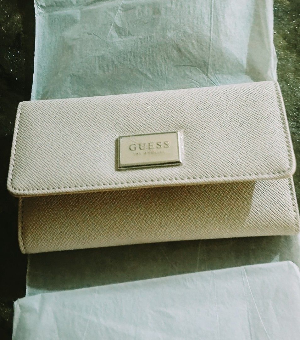 Guess beige trifold long wallet with multiple card slots (Category: Wallets & Card holders) located in Manila. Submitted by jazzsimpleme (Listing ID 1466374973, Image 2). Description: - Brand: Guess - Color: Neutral Beige - Material: Clean faux leather - Closure: Trifold with secure snap button - Interior: Multiple card slots on both flaps and a clear ID window - Storage: Plenty of space for cards and cash - Condition: Brand new / Excellent.