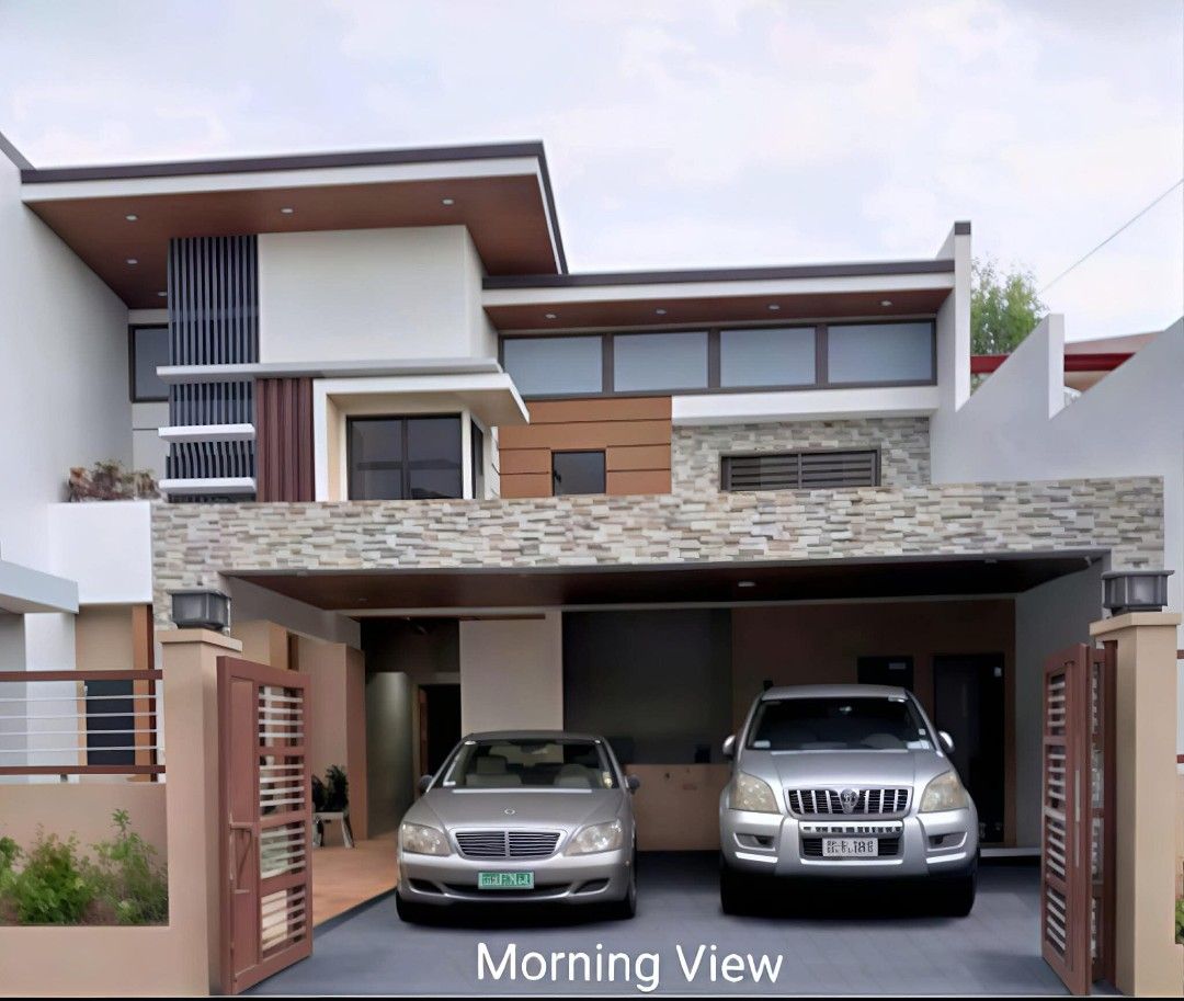 House For Sale (Category: House & Lot) located in Las Pinas. Submitted by mhay3188 (Listing ID 1466538472, Image 1). Description: Contemporary two-storey property. Includes a paved carport accommodating two vehicles, outdoor patio with landscaped planters, and ambient wall lighting. Interior spaces feature warm wood paneling, recessed ceiling lights, tiled floors, and an open layout dining area with built-in cabinetry. Clean finishes and modern a