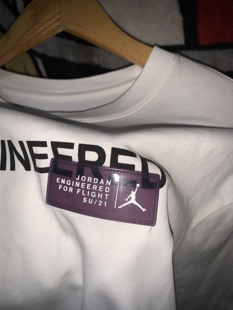 Jordan 23 Engineered White T-Shirt (Category: Tshirts & Polo Shirts ) located in Tayug. Submitted by cvcthrift (Listing ID 1466505417, Image 2). Description: 21/28 NO ISSUE EXCELLENT CR -9.5/10 - Brand: Jordan 23 Engineered - Color: White - Size: Small - Style Code: CZ5182-100 - Design: Black text graphic on chest with purple rubberized brand patch - Condition: Clean, print and patch are 100% intact with no cracks.