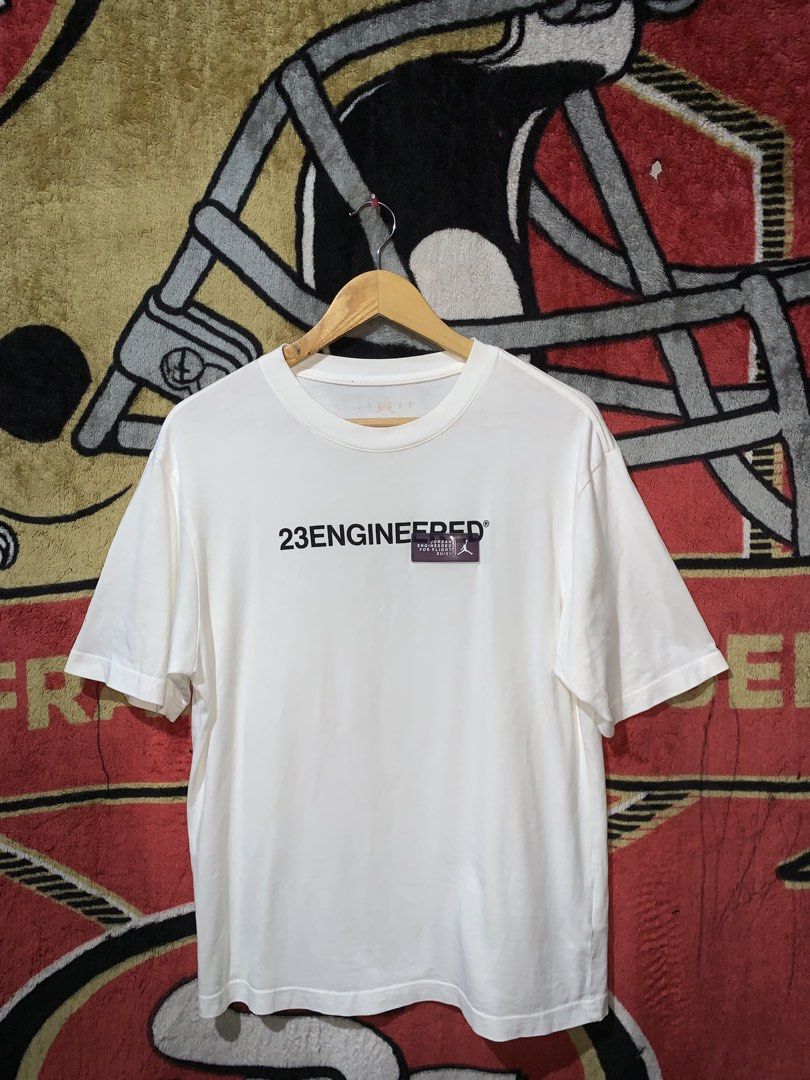 Jordan 23 Engineered White T-Shirt (Category: Tshirts & Polo Shirts ) located in Tayug. Submitted by cvcthrift (Listing ID 1466505417, Image 1). Description: 21/28 NO ISSUE EXCELLENT CR -9.5/10 - Brand: Jordan 23 Engineered - Color: White - Size: Small - Style Code: CZ5182-100 - Design: Black text graphic on chest with purple rubberized brand patch - Condition: Clean, print and patch are 100% intact with no cracks.