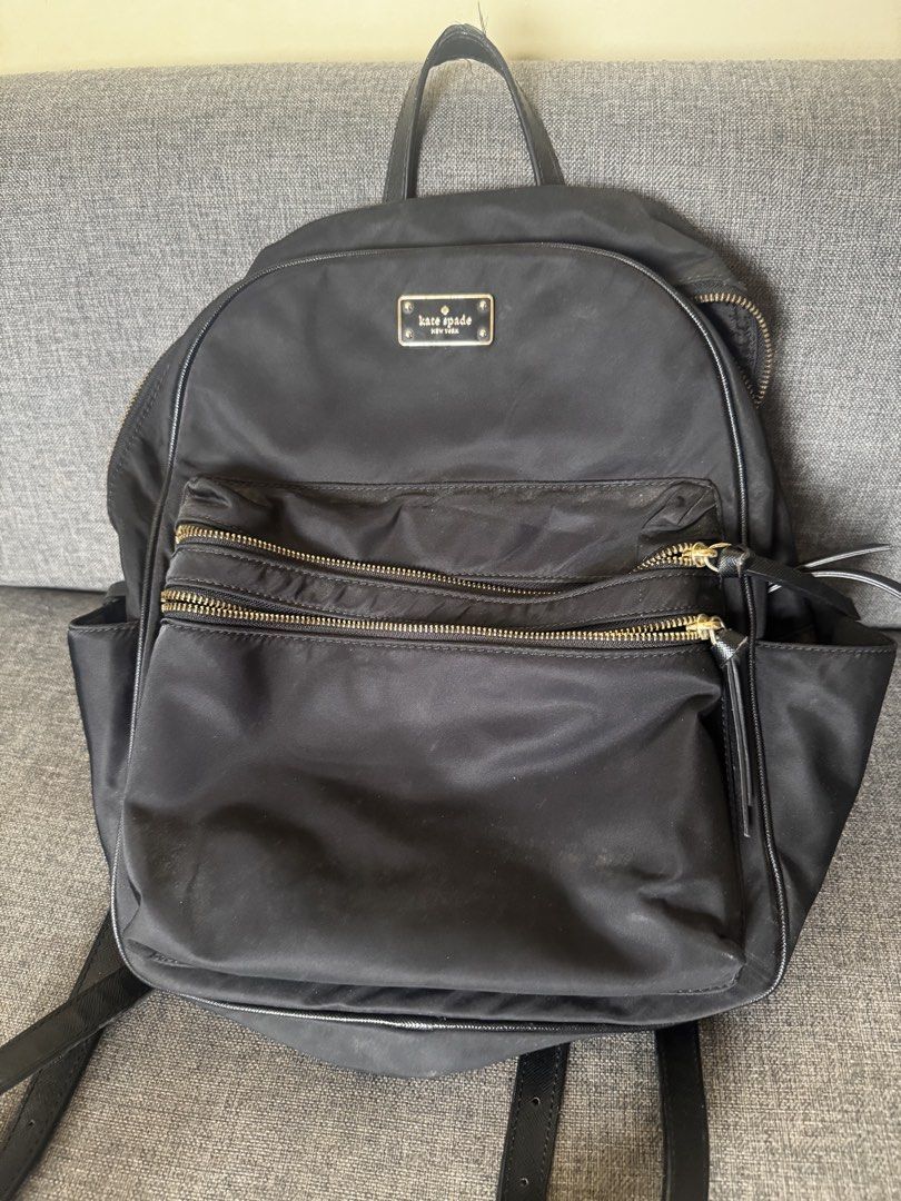 Kate Spade New York Black Nylon Backpack (Category: Backpacks) located in Noveleta. Submitted by rpalorma (Listing ID 1466337486, Image 1). Description: Black nylon backpack from Kate Spade New York. Gold-toned hardware, double zip front pockets, side slip pockets. Saffiano leather handle and adjustable straps. Signature printed lining inside with zip pocket and slip pockets. Shows noticeable wear and peeling on the top handle coating..