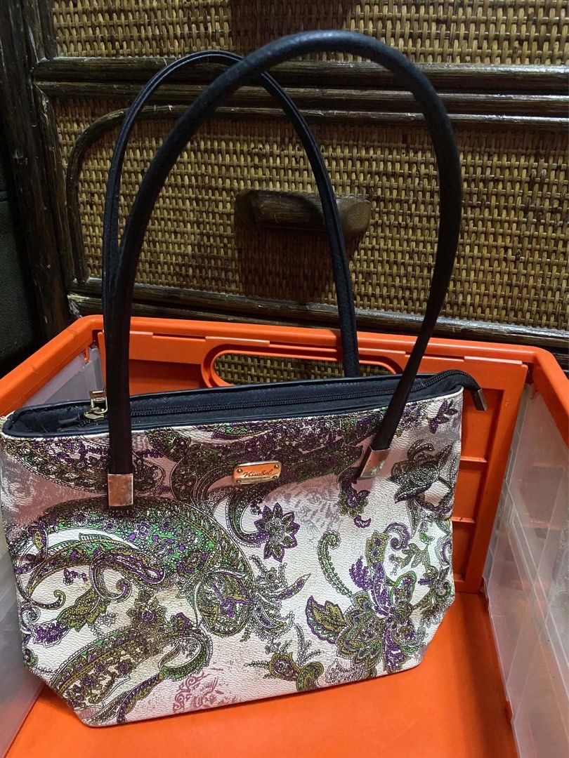 Kimbel International Patterned Tote Handbag (Category: Tote Bags) located in Manila. Submitted by catherinecafe (Listing ID 1466392553, Image 1). Description: - Brand: Kimbel International - Design: White base with intricate green, purple, and brown paisley floral patterns - Closure: Secure top zip closure - Straps: Dual black shoulder straps with stylish metallic connector hardware - Details: Front metallic Kimbel logo plaque - Interior: Clean l