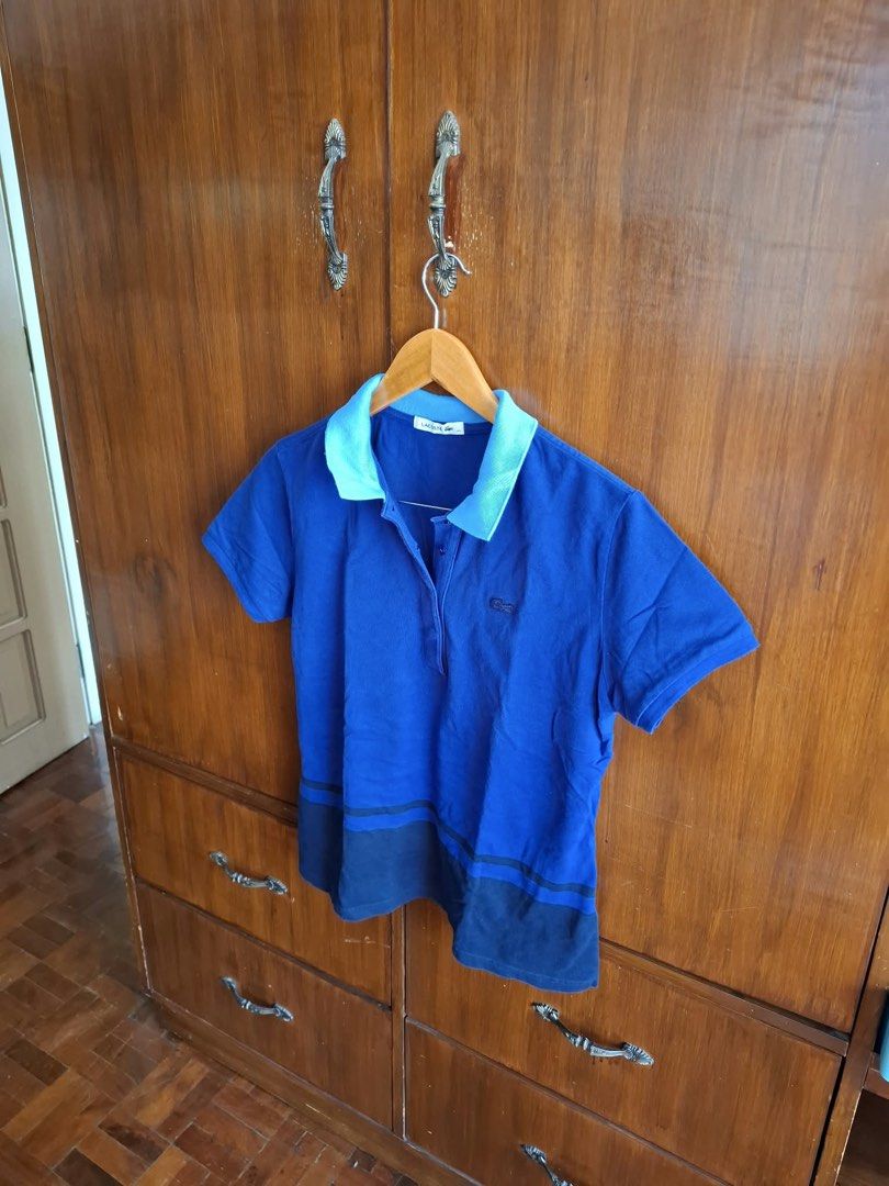 Lacoste Blue Polo Shirt Size 42 (Category: Tshirts & Polo Shirts ) located in Manila. Submitted by bunbun__ (Listing ID 1466414683, Image 2). Description: Lacoste women's polo shirt in blue with a lighter blue collar. Iconic crocodile logo embroidered on the left chest. Short sleeves with a button placket at the neckline. Bottom hem features a contrasting dark blue color block design. Clean stitching and classic cut. Great casual piece for everyd