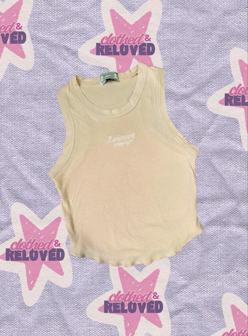 Leisure Beige Crop Top (Category: Sleeveless) located in Binan City. Submitted by szummie (Listing ID 1466466025, Image 1). Description: - Brand: Leisure - Color: Beige with white embroidered chest text - Material: Soft, stretchy cotton - Design: Scoop neckline, curved lettuce hem, cropped length.