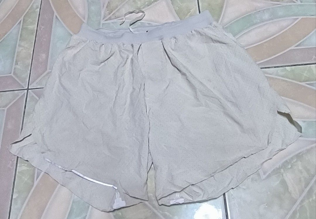 Lululemon Men's Athletic Shorts Size S (Category: Shorts) located in Manila. Submitted by itsmelawrence (Listing ID 1466357546, Image 2). Description: - Brand: Lululemon - Item: Men's Athletic Shorts - Size: S 26+ x 13 - Color: Light Grey - Material: Perforated fabric for maximum breathability - Features: Elastic waistband with adjustable drawstring, iconic silver reflective logo on lower hem - Condition: Excellent, great for running or gym sessi